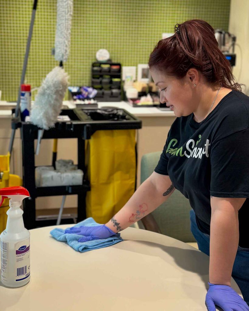 woman cleaning the top of a desk with disinfectant