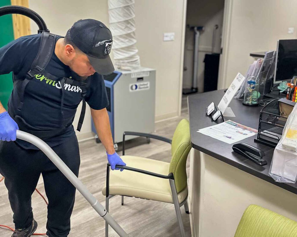 man vacuuming under a chair inside an office